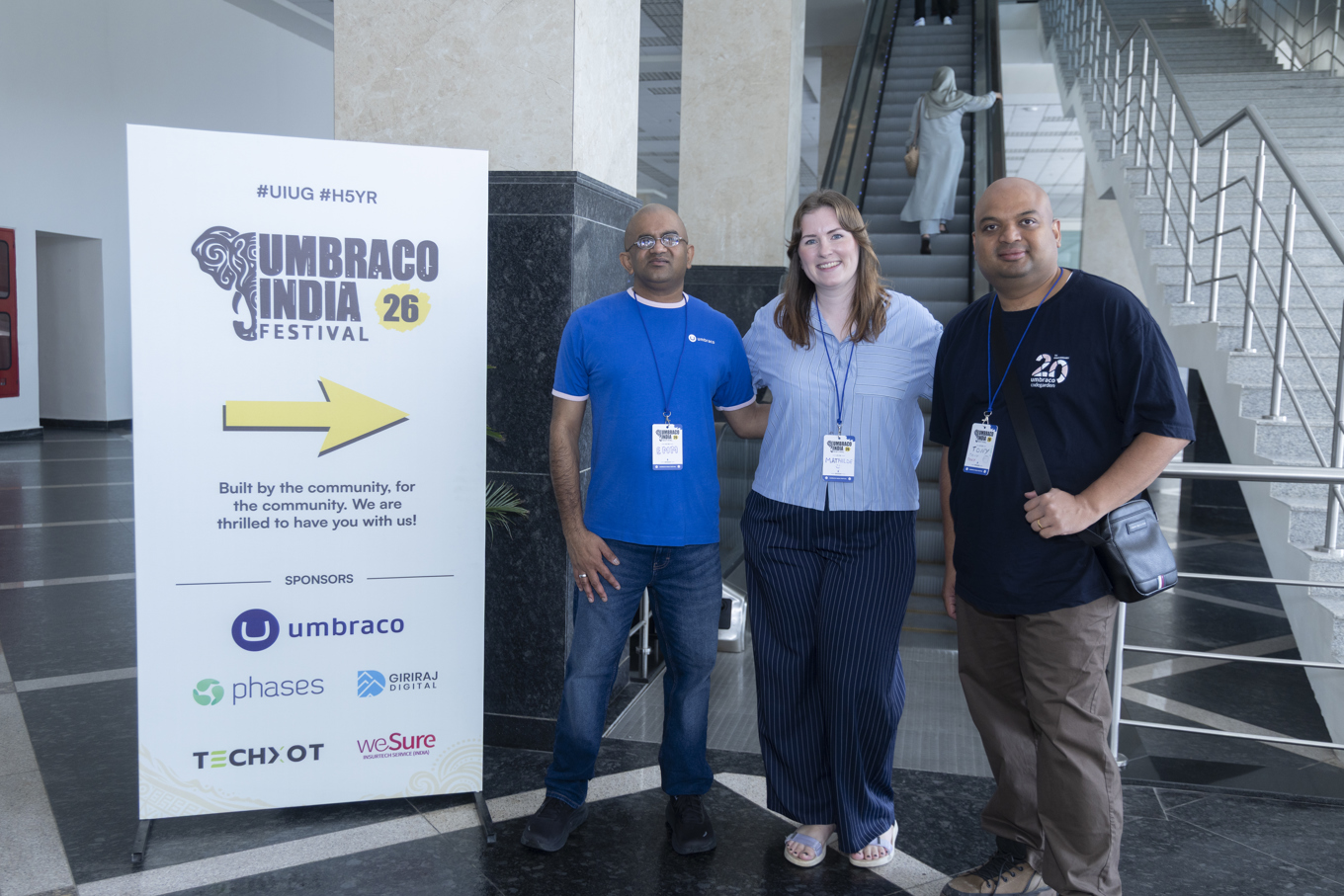 Three people standing next to a sign for Umbraco India Festival